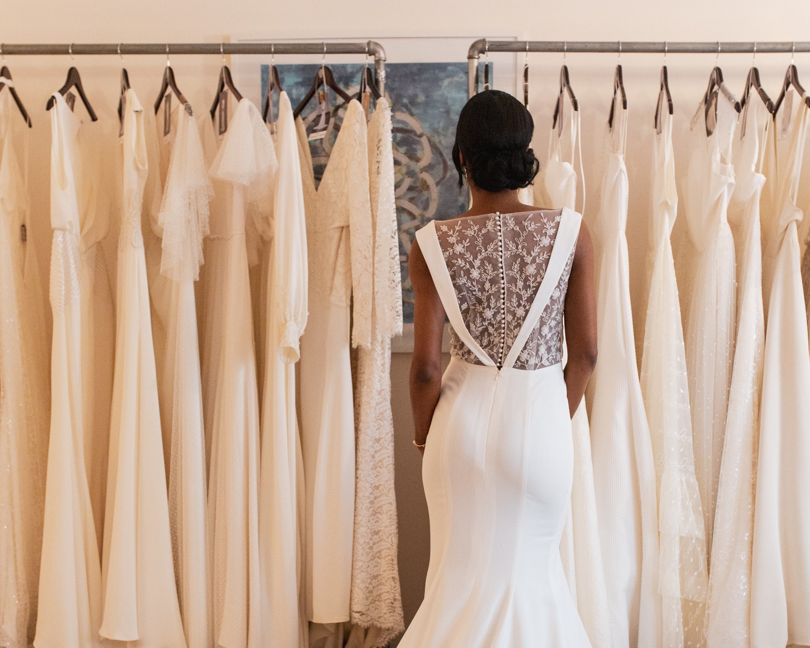 Model wears Edith Elan Jane wedding dress style while standing in front of dress racks