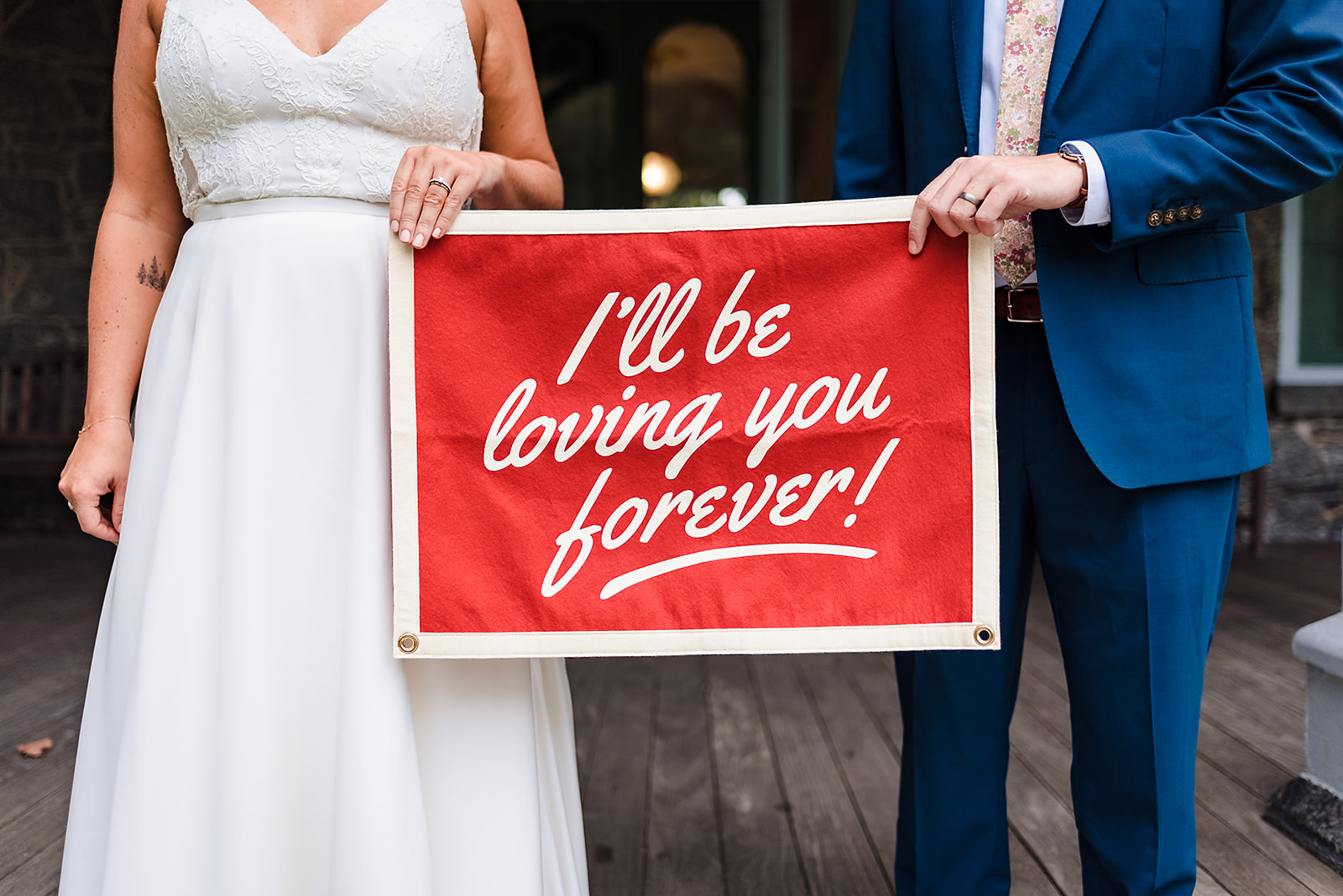 Bride and groom holding "I'll be loving you forever" banner