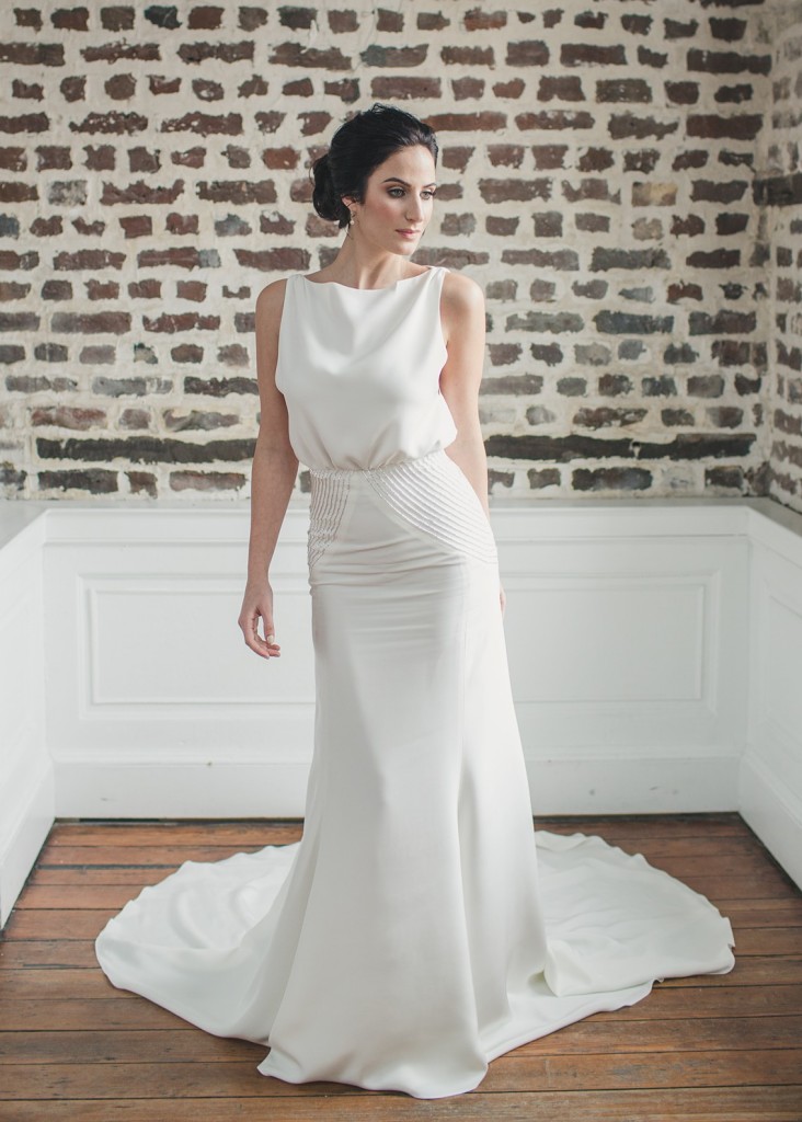 Heathe is a modern crepe wedding gown with a bateau neckline and keyhole back. The skirt hips are embroidered with rows of silver beads.
