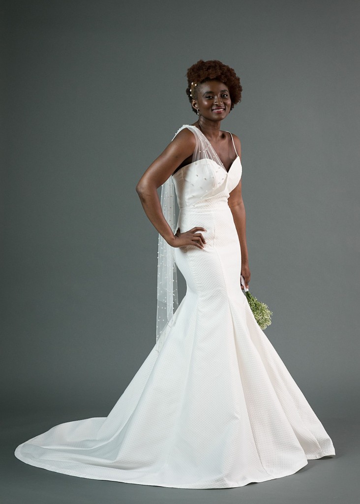 Mo by Edith Elan is an asymmetrical mermaid wedding dress in a textured dot jacquard fabric. The sweetheart neckline is accented with a draped pearl tulle scarf over the right shoulder.