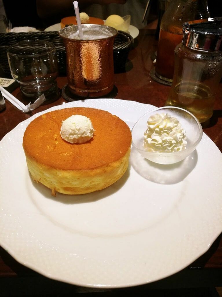 Single fluffy pancake with a dollop of butter served on a white plate with a side of whipped butter.