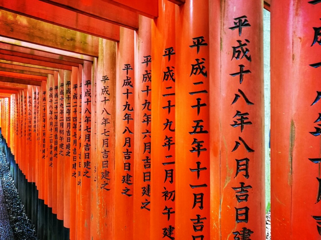 Black Japanese characters are carved into the orange torii gates.