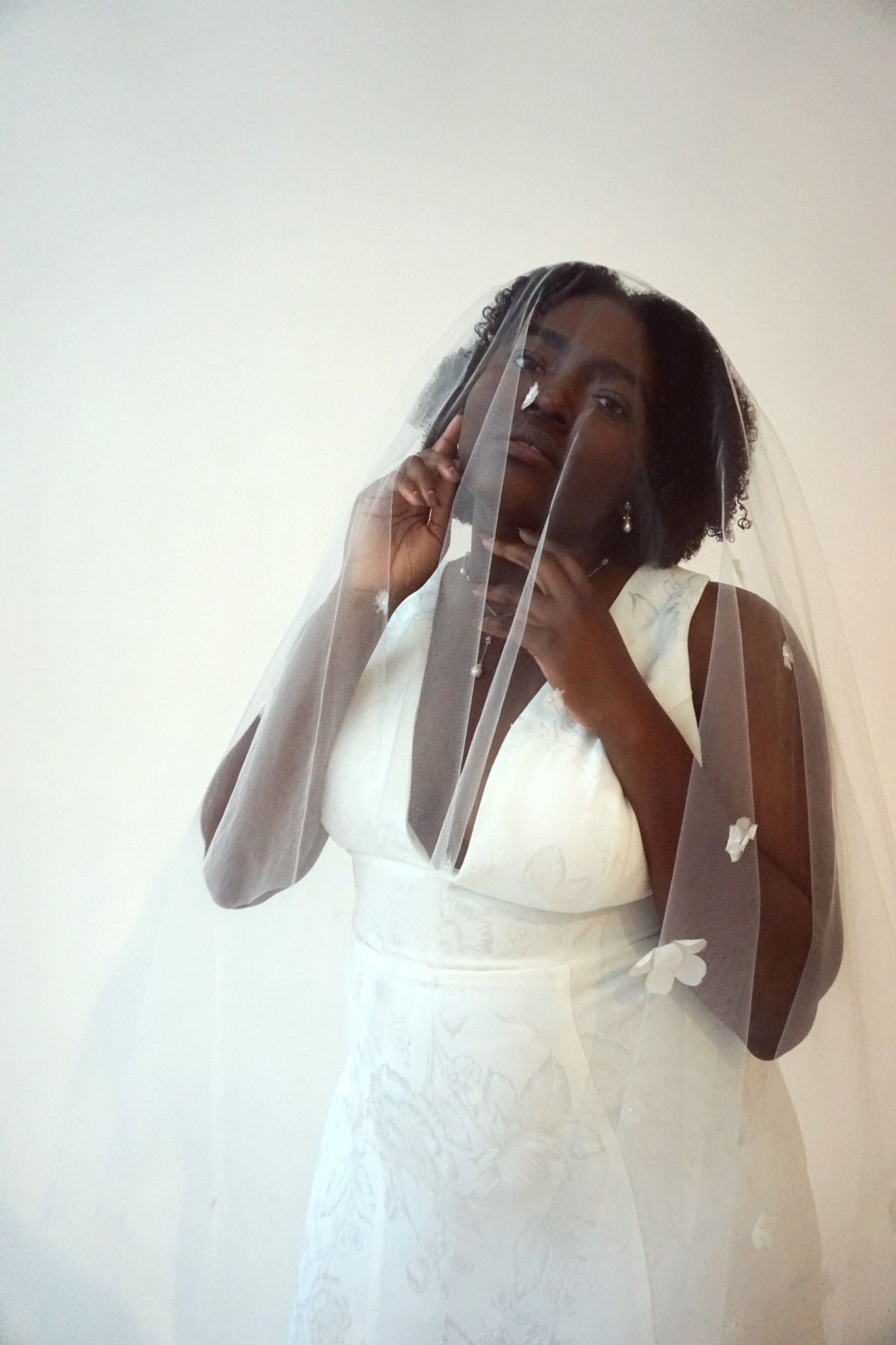 Black model wearing the Edith Élan Sol dress with a cathedral floral veil over her face.