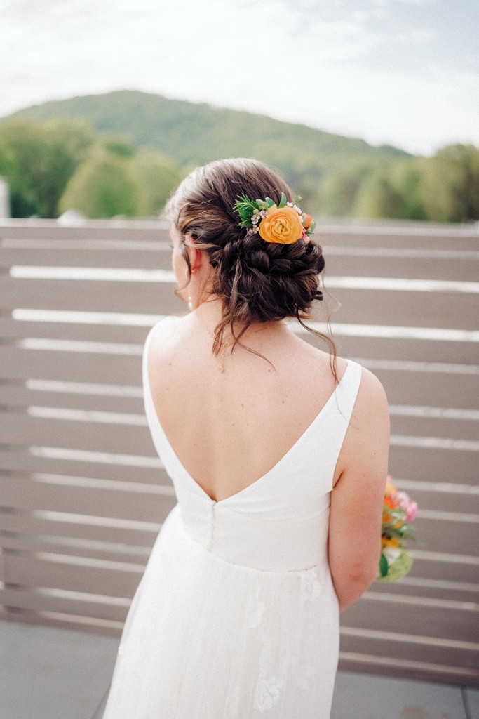 The bride's low bun hairstyle is adorned with a colorful floral spray to match her bouquet.