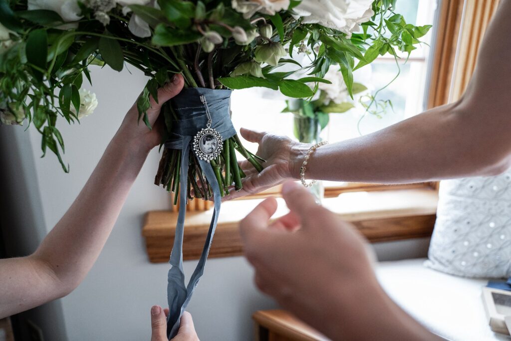 Pendant honoring the bride's late father pinned to her bridal bouquet's blue ribbon