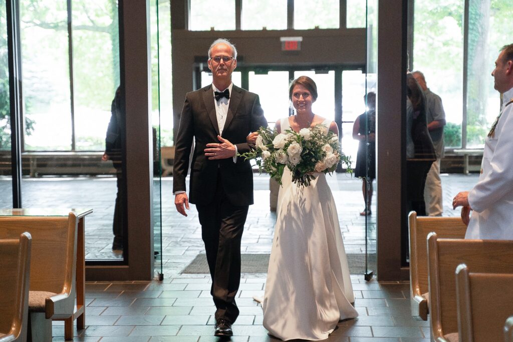The bride in her bespoke wedding gown by Edith Élan escorted in for the wedding ceremony