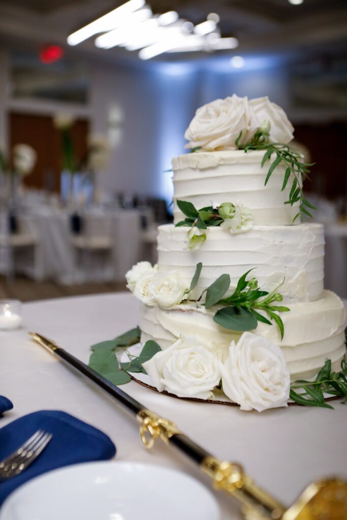 Three tier all white wedding cake decorated with white roses and greenery.