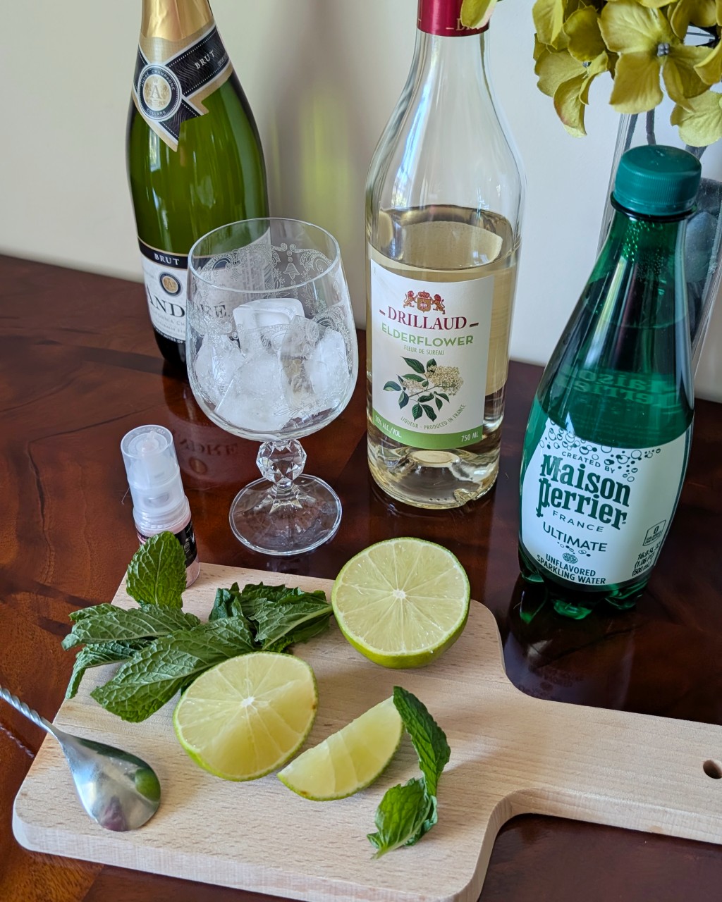 Ingredients for a Sparkling Spritz cocktail with brut, elderflower liqueur, lime, mint, sparkling water, and edible glitter.