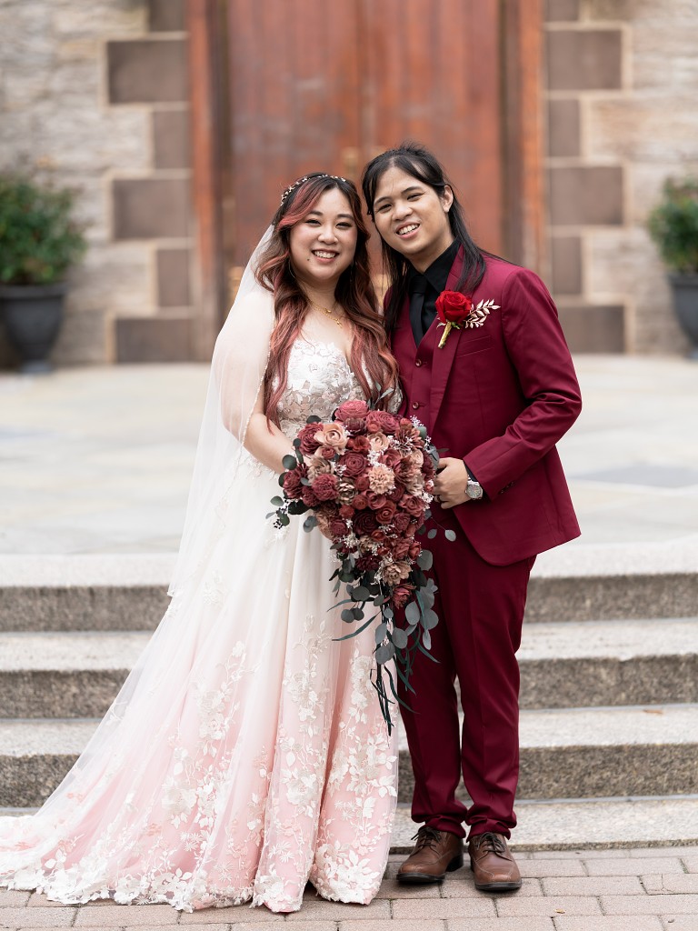 Couple in front of NYC Fordham University Church in a custom blush and lace wedding dress and a red suit.