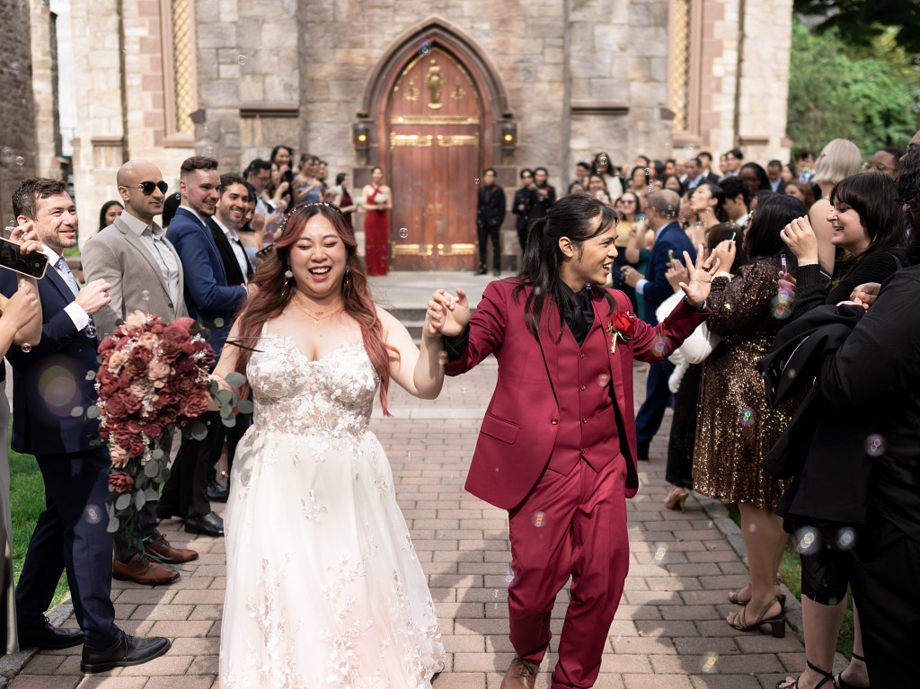 Bride and groom exit Fordham University Church after the wedding ceremony to guests blowing bubbles.