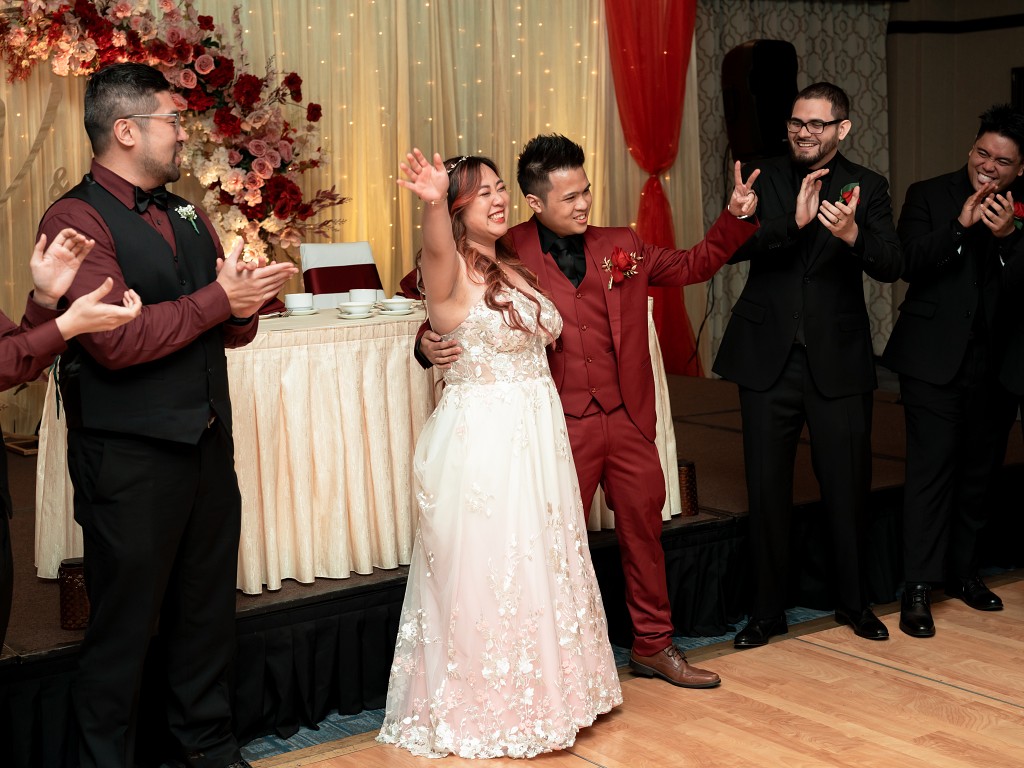 Bride in custom blush and lace wedding dress and groom in red and black suit during wedding reception introduction.